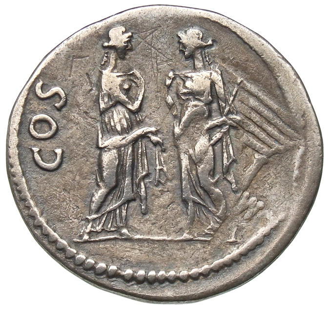 Hadrian reverse — Zwei Nemeseis stehen einander gegenüber. Die Figur r. hält in ihrer l. Hand eine Elle und die Figur l. in ihrer l. Hand die Zügel. Beide zupfen mit ihrer r. Hand jeweils ihr Gewand. Im r. F. sind Reste des Untertyps sichtbar (Tempel und die Aufschrift [C]OM).