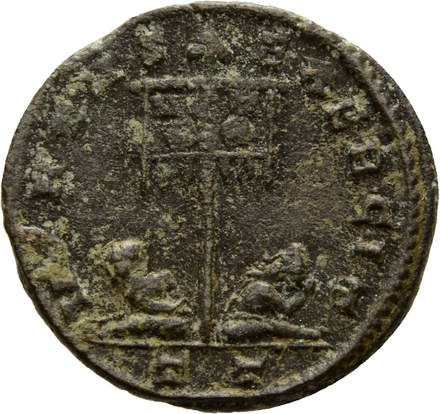 RIC VII Ticinum 116 Constantine I reverse, Standard with VOT/XX inscribed on drapery, flanked by two seated captives